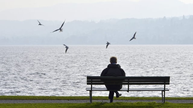 Ein Mann sitzt allein auf einer Bank am See.