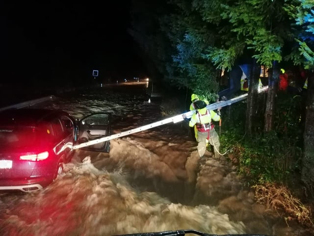 Einsatzkräfte scheinen einem Autofahrer oder einer Autofahrerin bei Hochwasser beim Aussteigen aus dem Auto zu helfen.