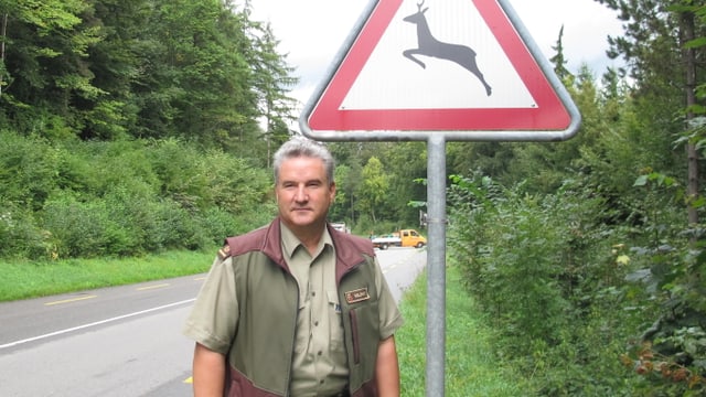 Ein Mann steht an einer Strassen vor einem Schild.