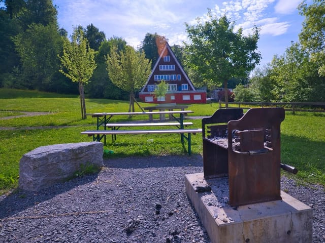 Park mit rustikalen Bänken und Haus im Hintergrund.