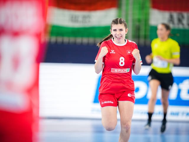 Glückliche Handballspielerin im roten Trikot auf dem Spielfeld.