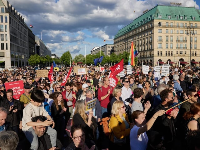 Demonstration auf einem grossen Platz mit Menschen, die Schilder und Fahnen halten.