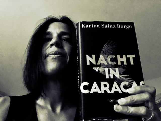 Annette König steht in einem dunklen Raum und hält Karina Sainz Borgos Roman «Nacht in Caracas» in die Kamera