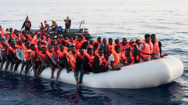 Flüchtlinge mit Westen auf einem Gummiboot.