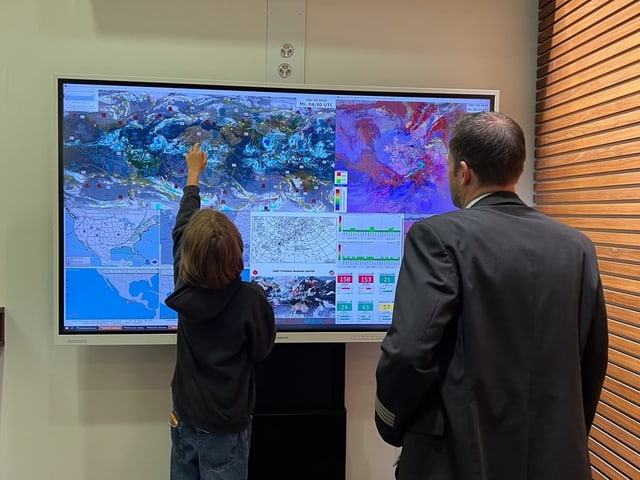 Zwei Menschen stehen vor einem grossen Bildschirm mit verschiedenen Wetterprognosen. 