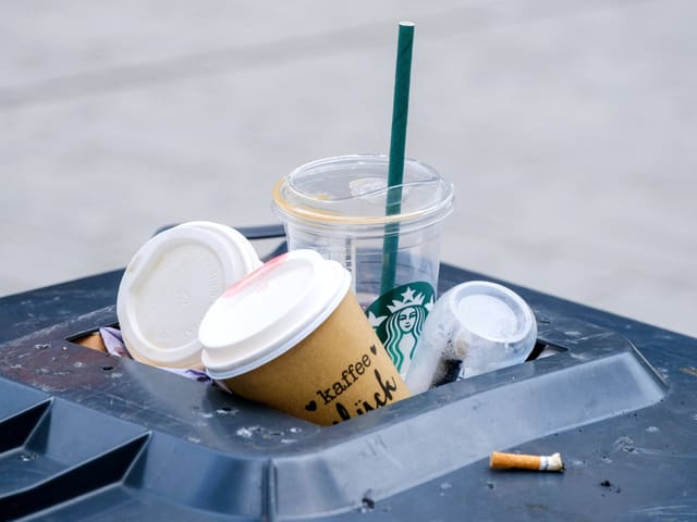 Mülltonne mit Kaffeebechern und Zigarettenstummel.