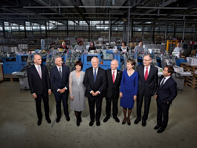 Die Mitglieder des Bundesrates stehen in einer Fabrikhalle.