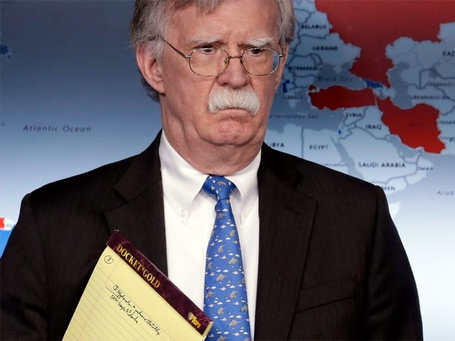 John Bolton mit ernstem Blick und dem gelben Notizblock unter dem Arm.