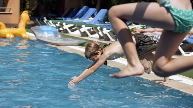 Zwei Kinder springen ins Schwimmbecken. 