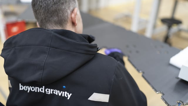 Person mit schwarzer Beyond Gravity-Jacke am Arbeitstisch.