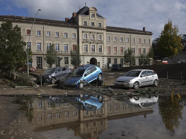 Schlammige Strasse mit beschädigten Autos vor einem grossen Gebäude.