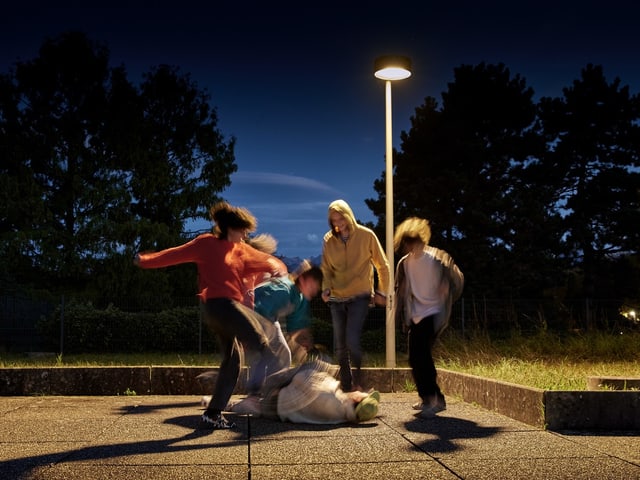 Kinder spielen bei Nacht im Freien unter einer Strassenlaterne.