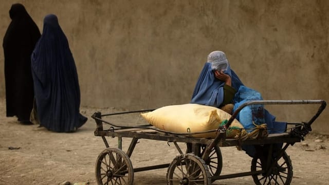 Afghanische Frau sitzt auf einem Wagen mit einem Sack, der mit Hilfsgütern gefüllt ist.