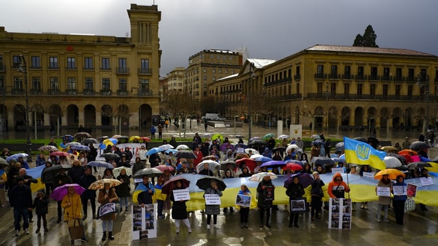 Menschen mit bunten Regenschirmen und blau-gelben Ukraine-Flaggen.