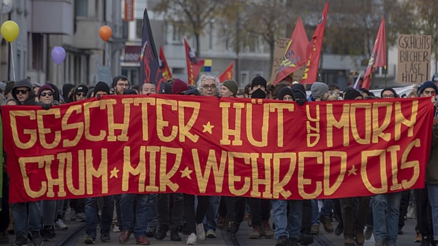 Eine Gruppe Menschen läuft mit einem Banner durch Basels Strassen. 