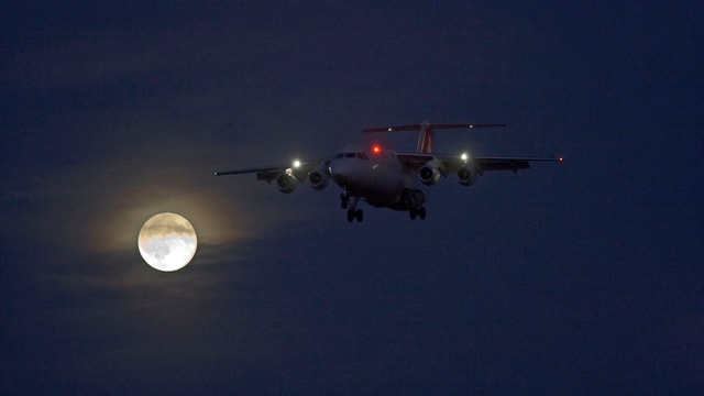 Die Lichter eines Flugzeugs in der Luft, im Hintergrund Vollmond. 