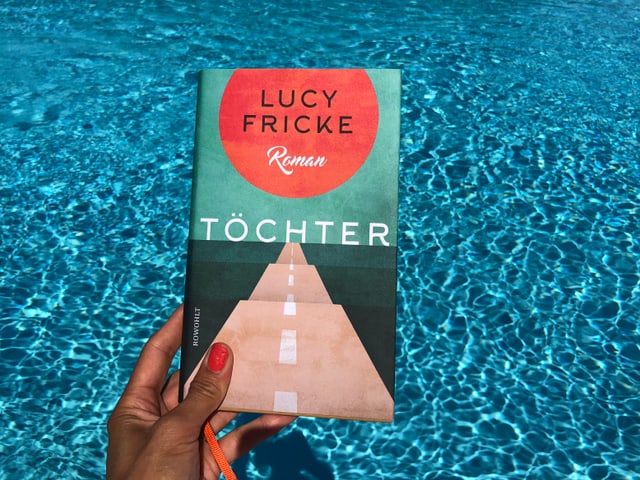 Annette König hält das Buch von Lucy Fricke: «Töchter» vor blaues Wasser