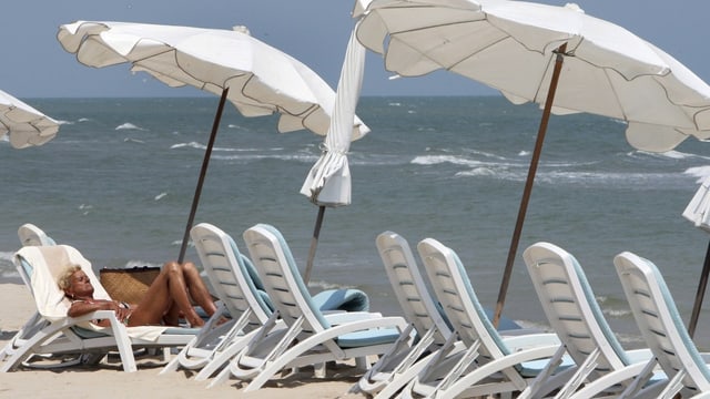 Ältere Frau in einem Sonnenstuhl am Strand.