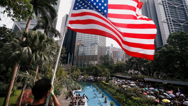 Mann schwenkt US-Flagge, dahinter der Demonstrationszug.