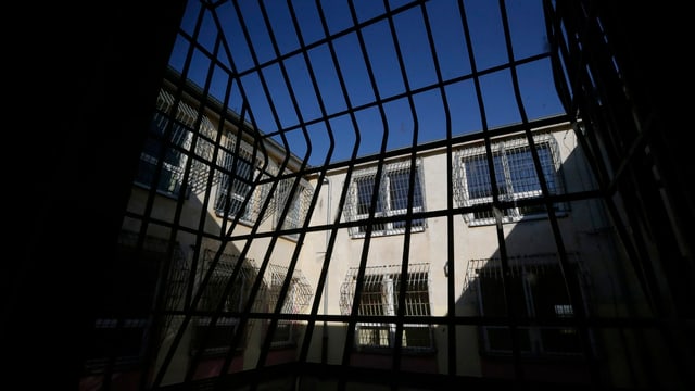 Blick in einen vergitterten Gefängnis-Innenhof, weit oben ein Stückchen blauer Himmel.