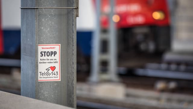 Ein Aufkleber auf einem Stahlträger neben Bahngleisen, der auf Seelsorge-Hilfe hinweist.