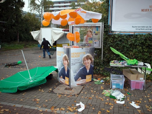 Wahlkampfstand, darauf ein Plakat der Frau. Es herrscht ein Durcheinander.