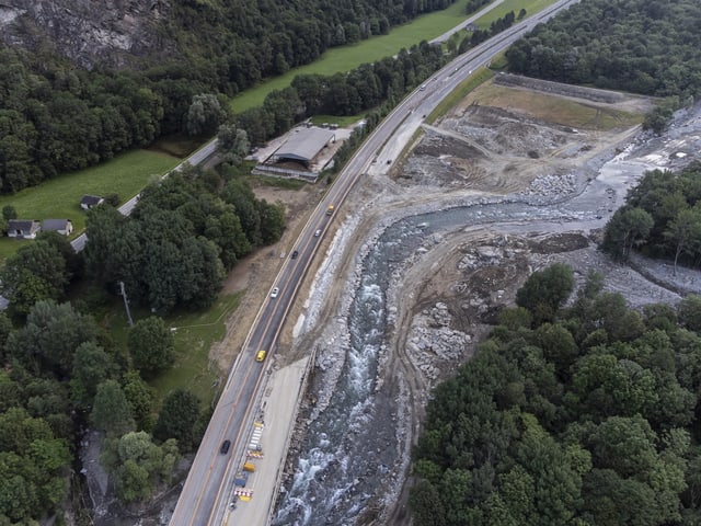 Luftaufnahme einer Strasse neben einem Fluss mit umliegenden Bäumen und Gebäuden.