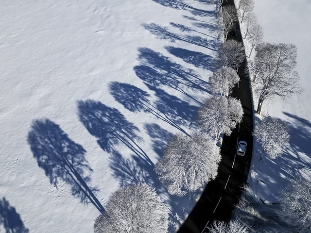 Ein Auto fährt auf einer Strasse durch die Schneelandschaft.