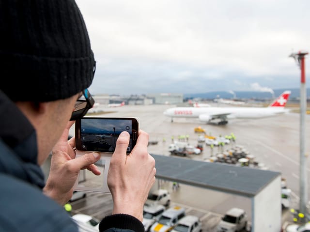 Mann mit Handy fotografiert Flugzeug.