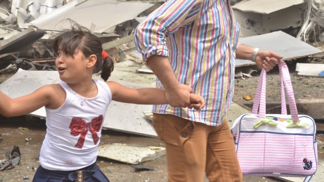 Frau hält in einer mit Trümmern übersähten Strasse von Aleppo ein Kind in weissem T-Shirt an der Hand