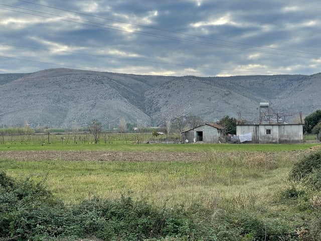 Ein Feld, das landwirtschaftlich genutzt wird. Etwas weiter hinten: zwei heruntergekommene Gebäude.