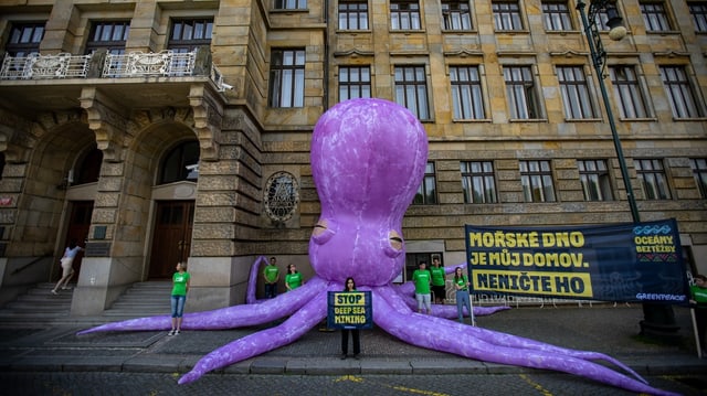 Ein grosser, violetter Tintenfisch vor einem Gebäude. Mehrere Menschen mit Plakaten stehen davor.