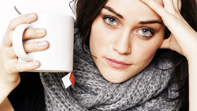 Junge Frau hat den Kopf aufgestützt und schaut direkt in die Kamera, in der Hand eine grosse Teetasse.