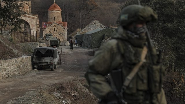 Russischer Soldat, unscharf, steht an einer Strasse, dahinter eine kleine Kapelle, scharf.