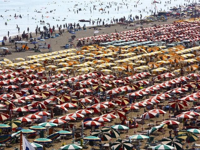 Proppenvoller Sandstrand mit Sonnenschirmen dicht an dicht.