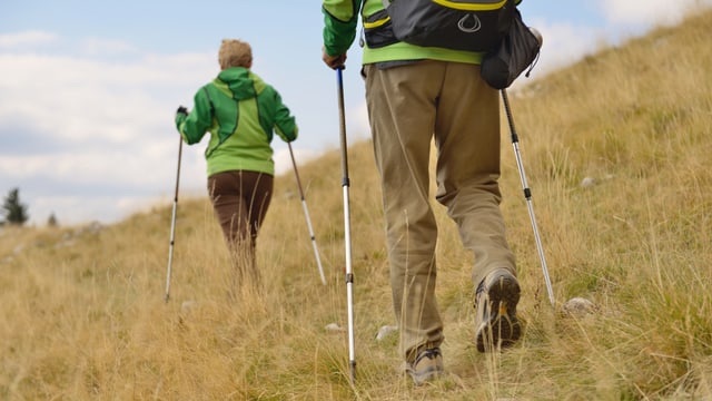 Zwei Wanderer mit Trekkingstöcken erklimmen einene Berg