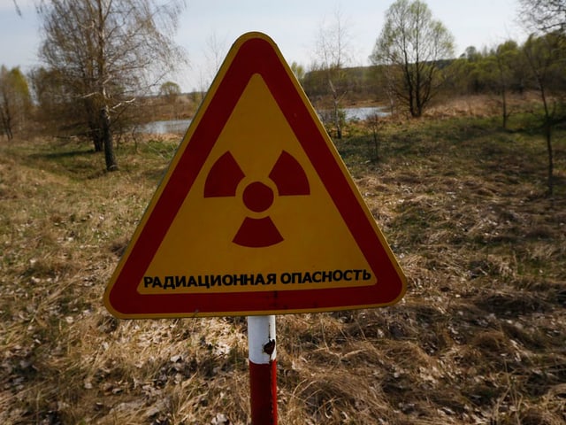 Warnschild Atomstrahlung, dahinter eine karge Landschaft