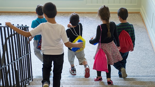 Kinder mit bunten Schultaschen laufen eine Treppe hinunter.