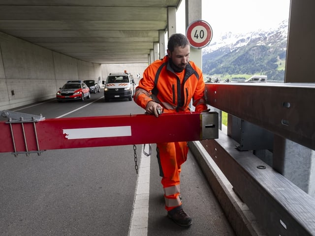 Mann in Arbeitsanzug öffnet Schranke.