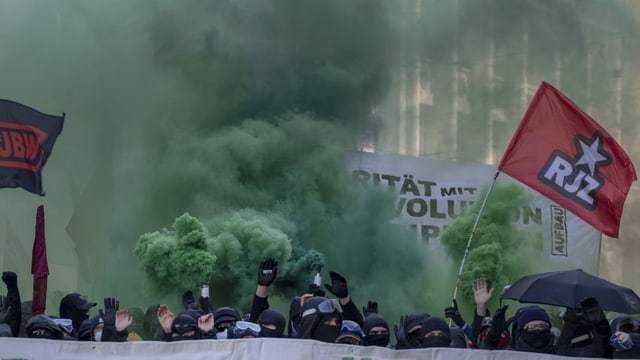 Vermummte Gesichter während der Demonstration in Basel. Rechts ist eine fahne der Revolutionären Jugend Zürich zu sehen.