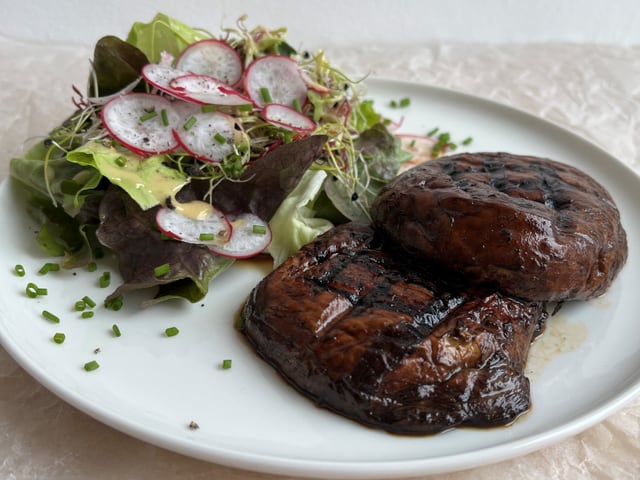 Gebratene, marinierte  Portobello-Pilze und Salat auf einem weissen Teller.