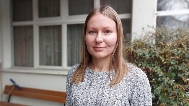 Frau mit langen blonden Haaren und Wollpullover vor einem Fenster.