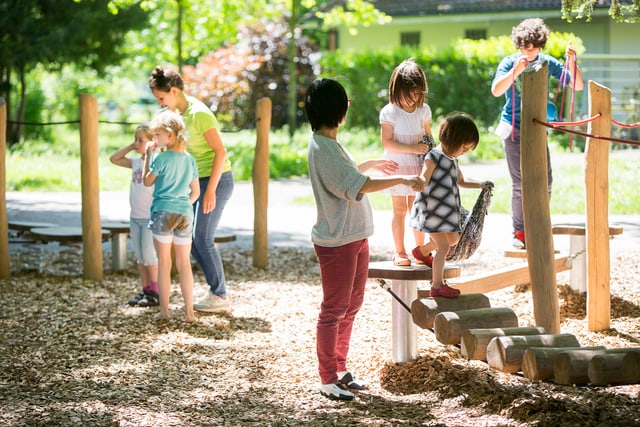 Kinder gehen über einen wackeligen Weg, die Mutter unterstützt. 