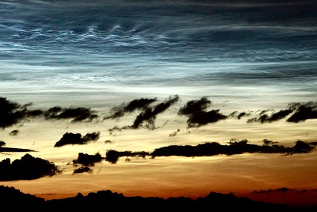 Silbern leuchtende Nachtwolken am dunklen Himmel.