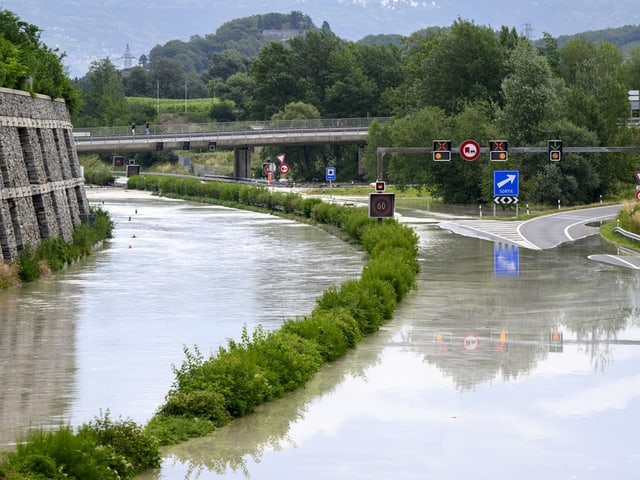 Überflutete Strasse entlang eines Kanals mit Verkehrsschildern.