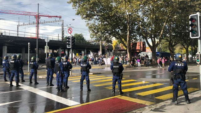 Police officers stand on the street in front of the protesters.