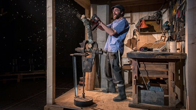 Ein Schauspieler schnitzt eine Puppe aus Holz.