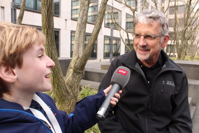 Ein Junge streckt einem Mann ein Mikrofon hin und dieser spricht rein.