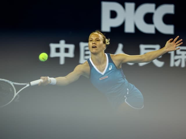 Tennisspielerin streckt sich nach einem fliegenden Ball auf einem Tennisplatz.