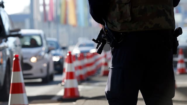 Polizist mit gesenkter Waffe neben Autokolonne